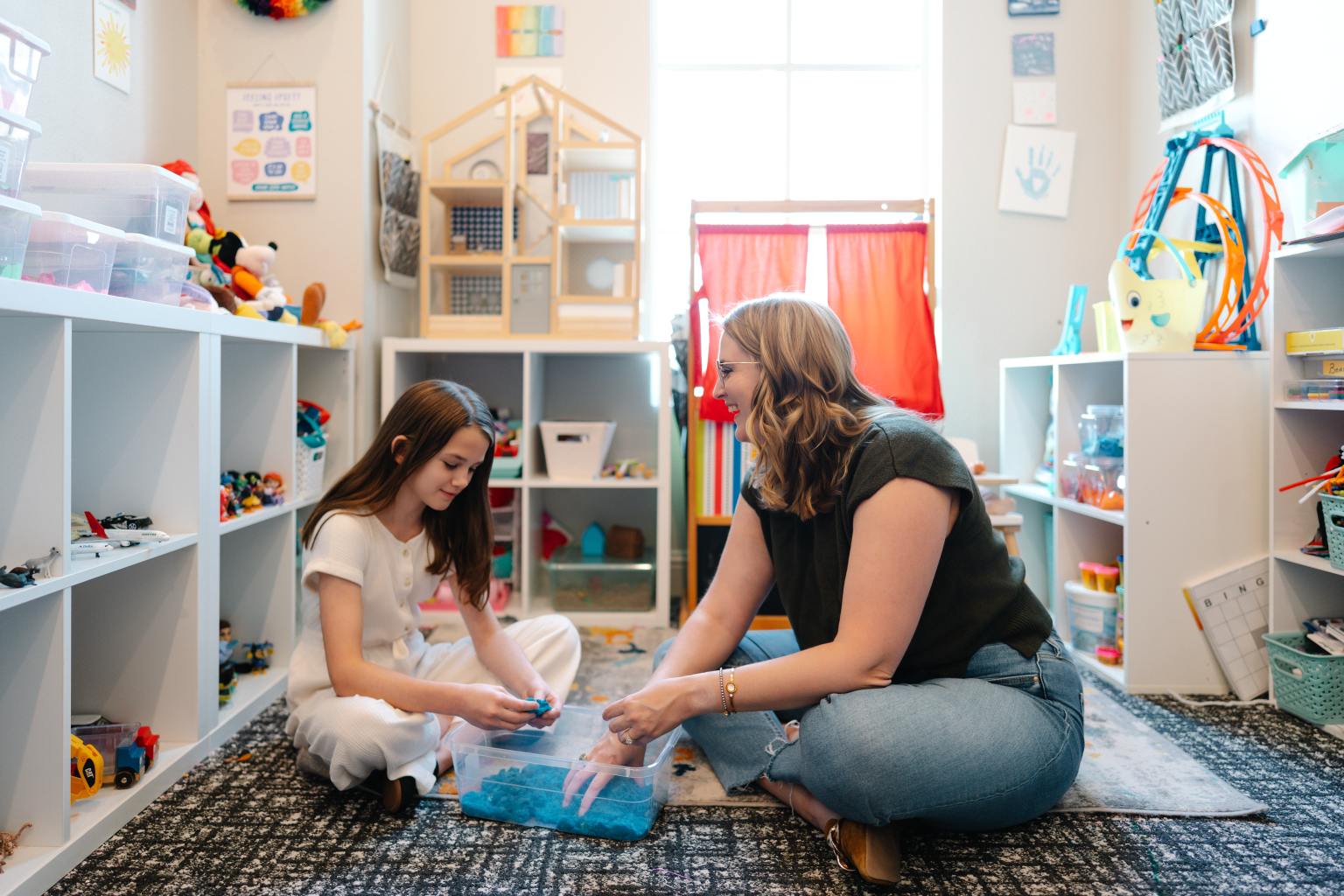 A wide view of the play therapy room, set up with low open shelves and a sand tray